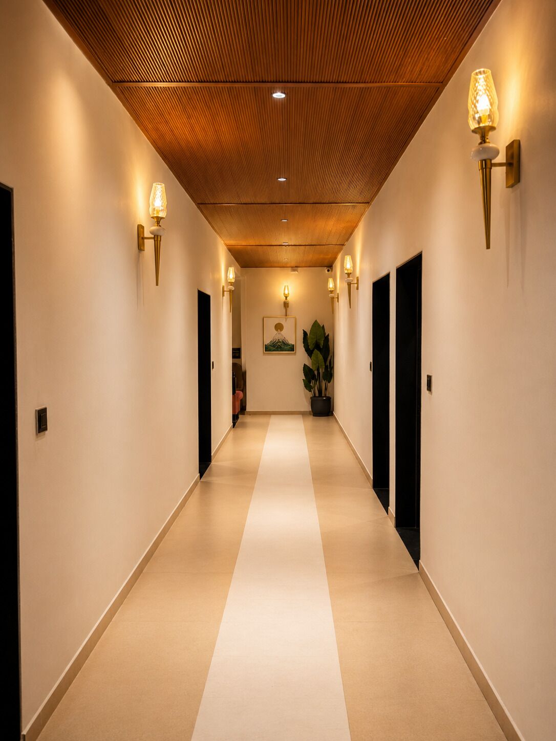 Un pasillo de hotel con techo de madera, luces empotradas en la pared, una planta y un cuadro enmarcado.