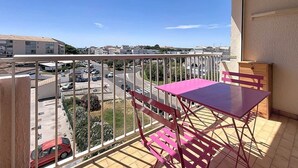 Ein Balkon mit Tisch und Stühlen, Blick auf einen Parkplatz und Gebäude im Hintergrund.
