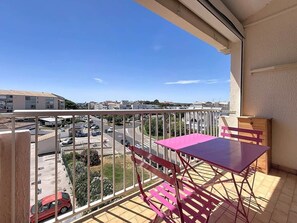 Ein Balkon mit Tisch und Stühlen, Blick auf einen Parkplatz und Gebäude im Hintergrund.