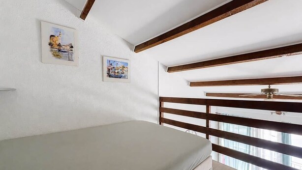 Ein Schlafzimmer mit einem Bett, Holzbalken, einem Deckenventilator und zwei gerahmten Bildern an der Wand.