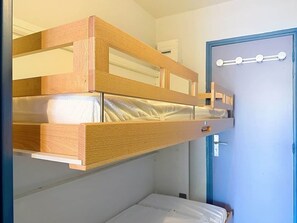 Un lit superposé avec une structure en bois et un matelas. Il y a une porte avec un interrupteur sur le mur.