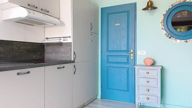 Een keuken met witte kasten, een blauwe deur en een kleine dressoir met lades.