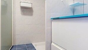 Een badkamer met witte betegelde wanden, een blauw betegelde douchevloer, een witte wastafel met een zeepdispenser en een glazen plank aan de muur.