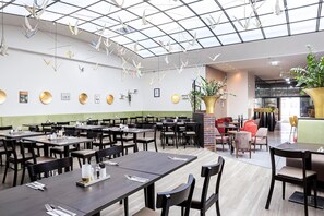 Ein großzügiges Restaurant mit mehreren Tischen und Stühlen, einem modernen Deckenbau und einer grünen Wand mit runden Verzierungen.
