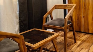 Una habitación con un armario de madera, dos sillas de madera con cojines y una mesa de vidrio.