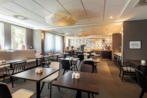 Een moderne eetruimte met meerdere tafels en stoelen, een bar op de achtergrond en een wand met een patroon.