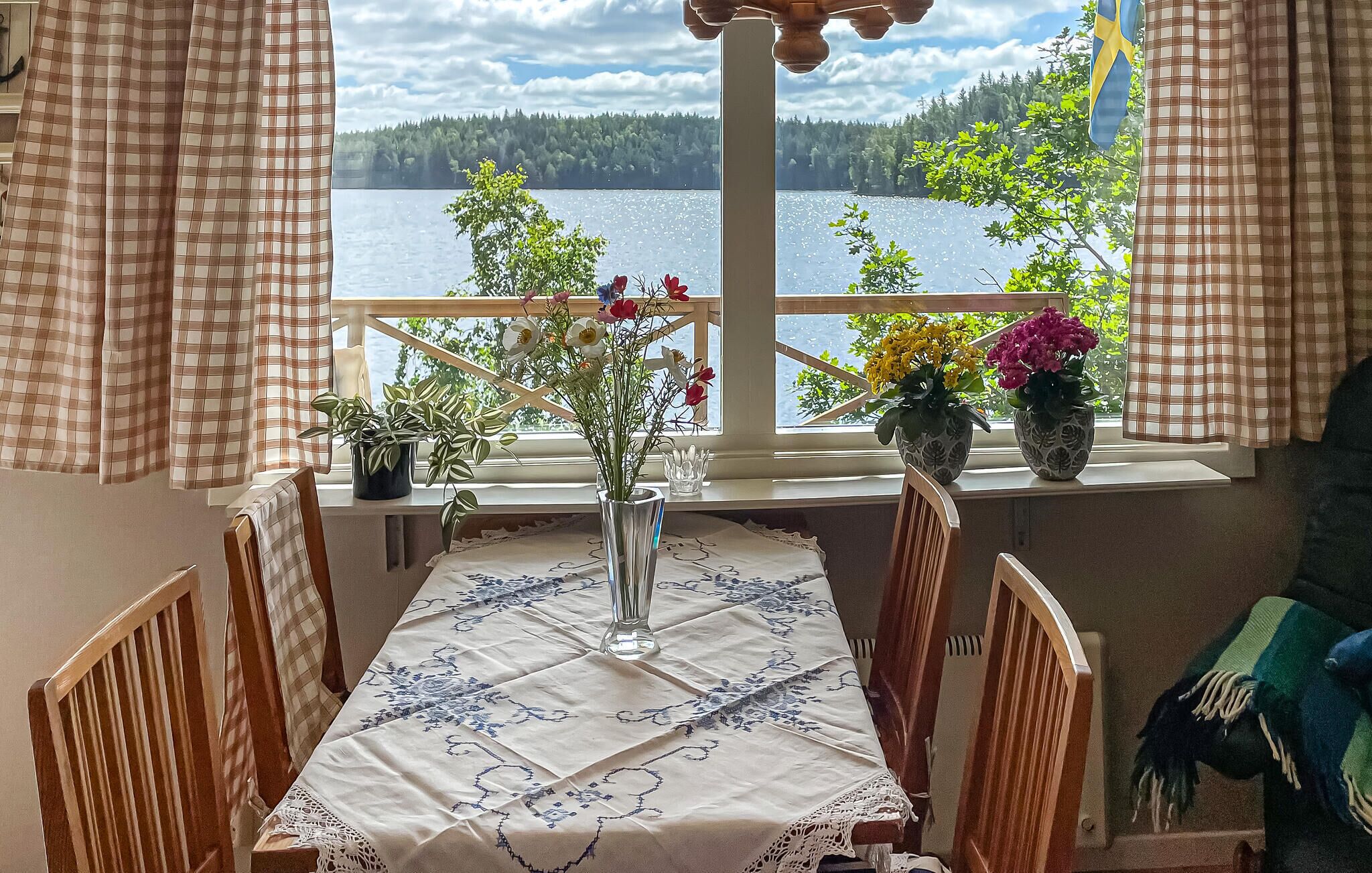 Un coin repas avec une table dressée pour quatre personnes, une vue sur un lac et des plantes en pot sur le rebord de la fenêtre.