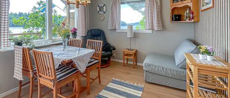 Habitació acollidora amb taula de dinar, cadirees, sofà, taula auxiliar petita i finestra amb cortines.