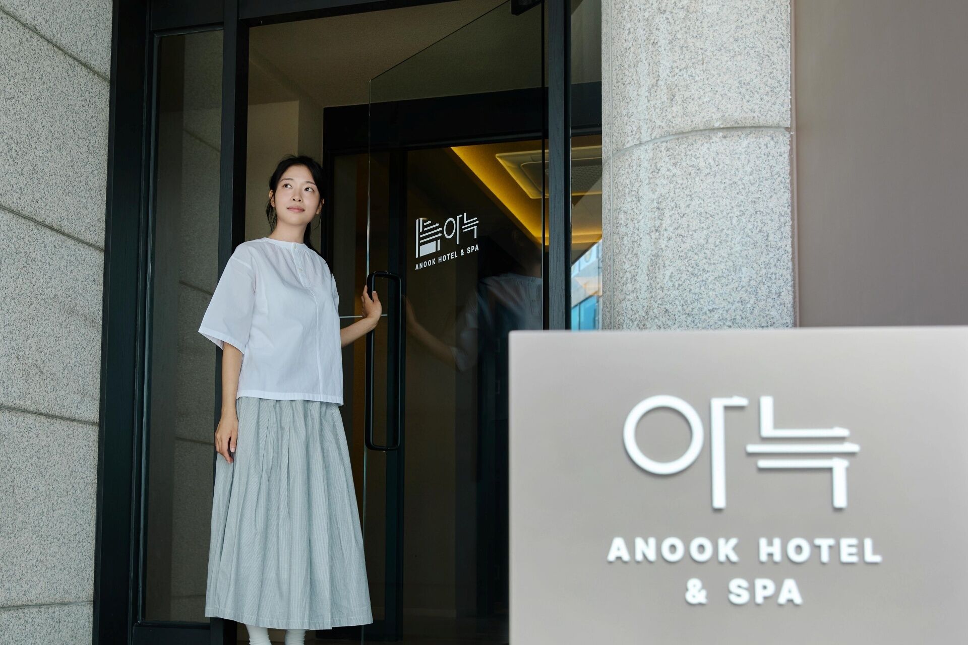 A person standing at the entrance of Anook Hotel & Spa, with a signboard displaying the hotel's name.