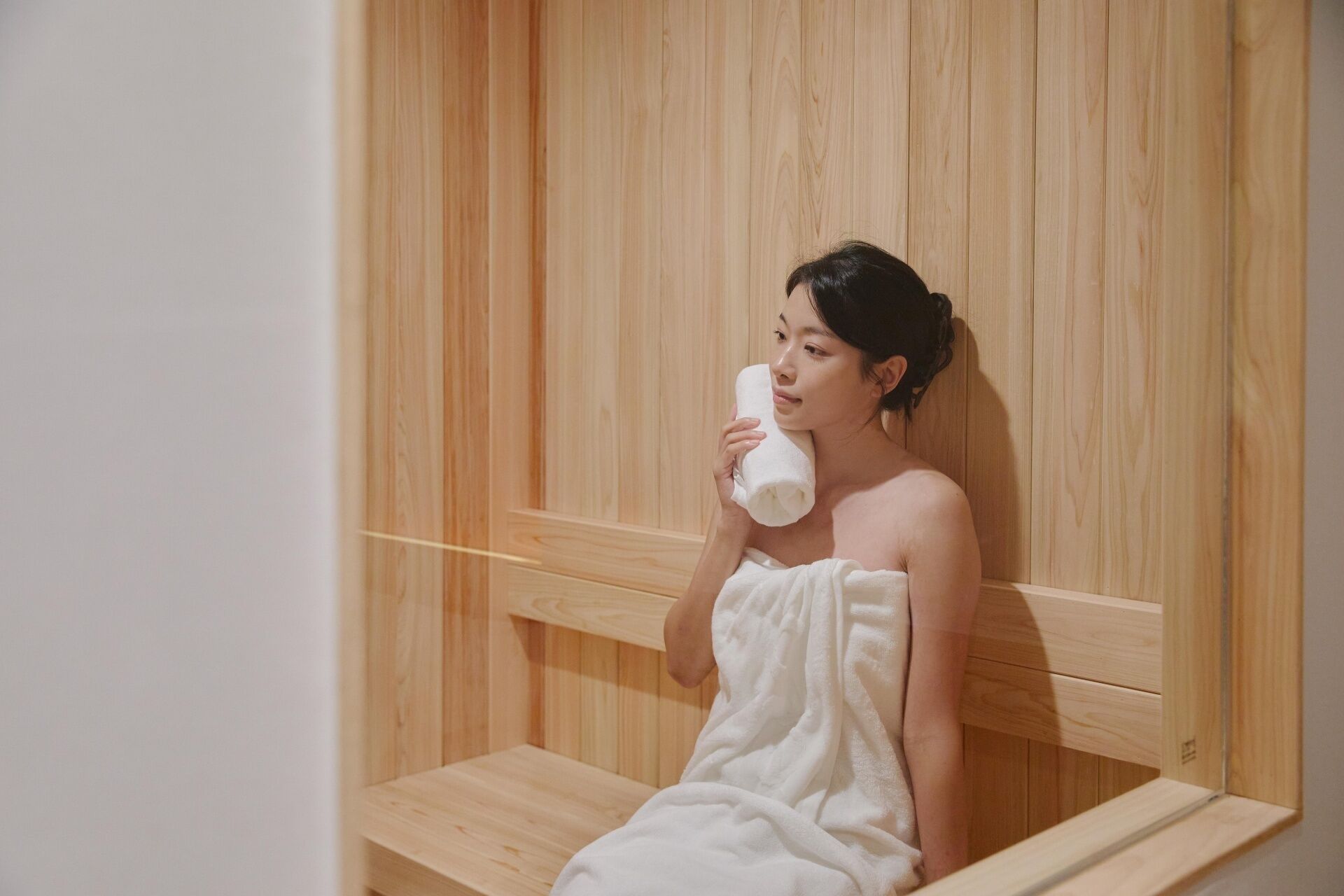 A person sitting in a wooden sauna with a towel wrapped around their body.