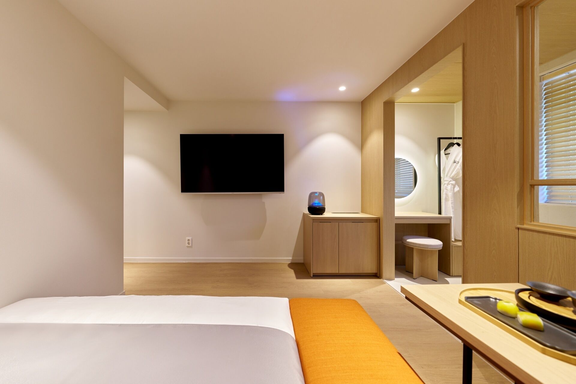 A modern hotel room with a bed, a TV, a small desk, and a bathroom visible through an open door.