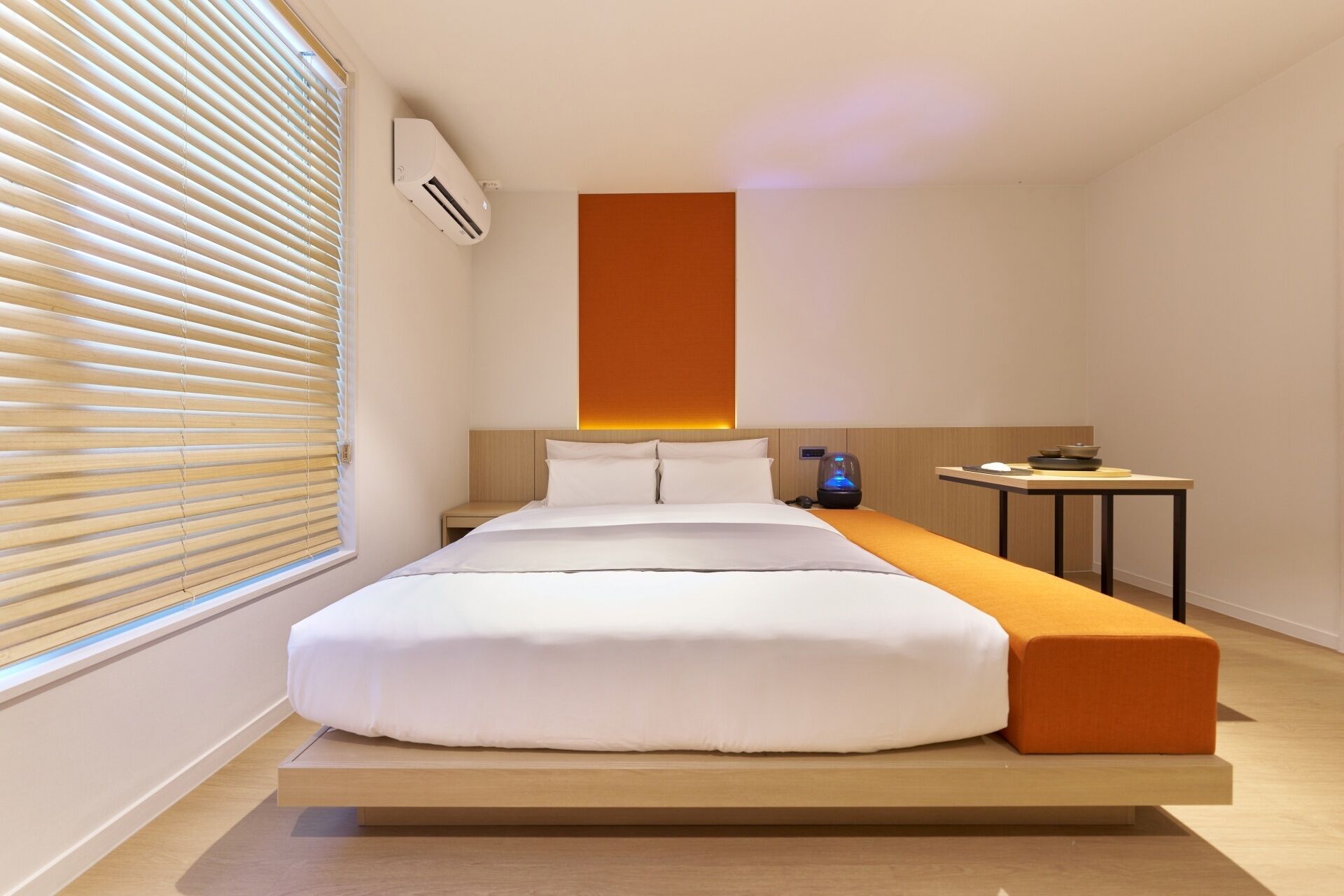 A modern hotel room with a bed, bedside table, and a small table with a lamp.