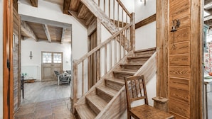 Una escalera de madera que sube a un segundo piso, una silla de madera y una puerta con un cascabel.