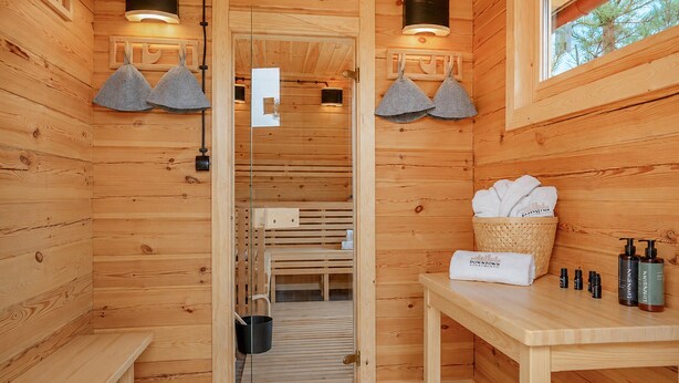 Una cabaña de madera con sauna, una banca, una mesa con toallas y artículos de aseo.