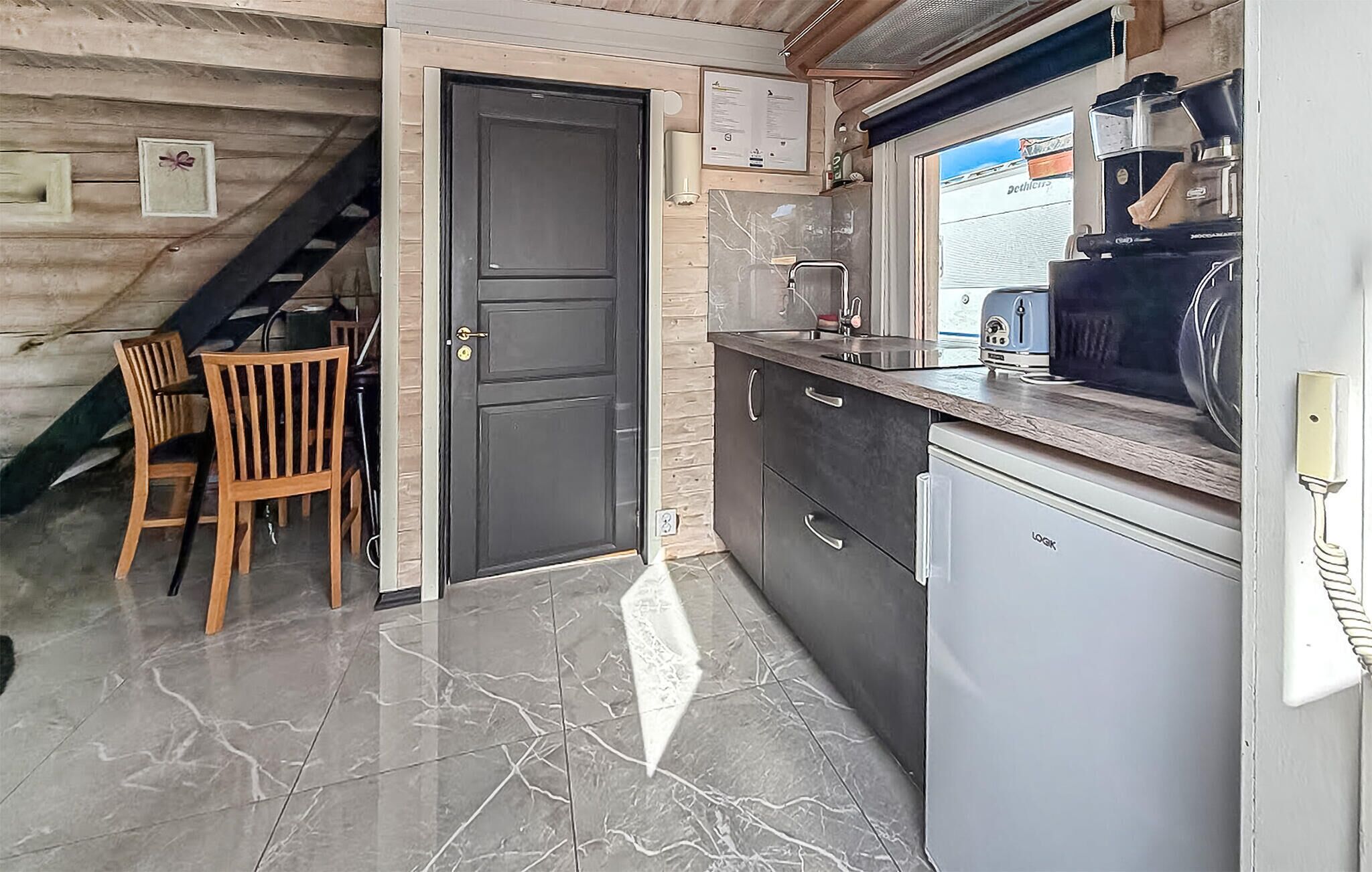 A kitchen with a dark door, a small refrigerator, and a window with a view of the sea.