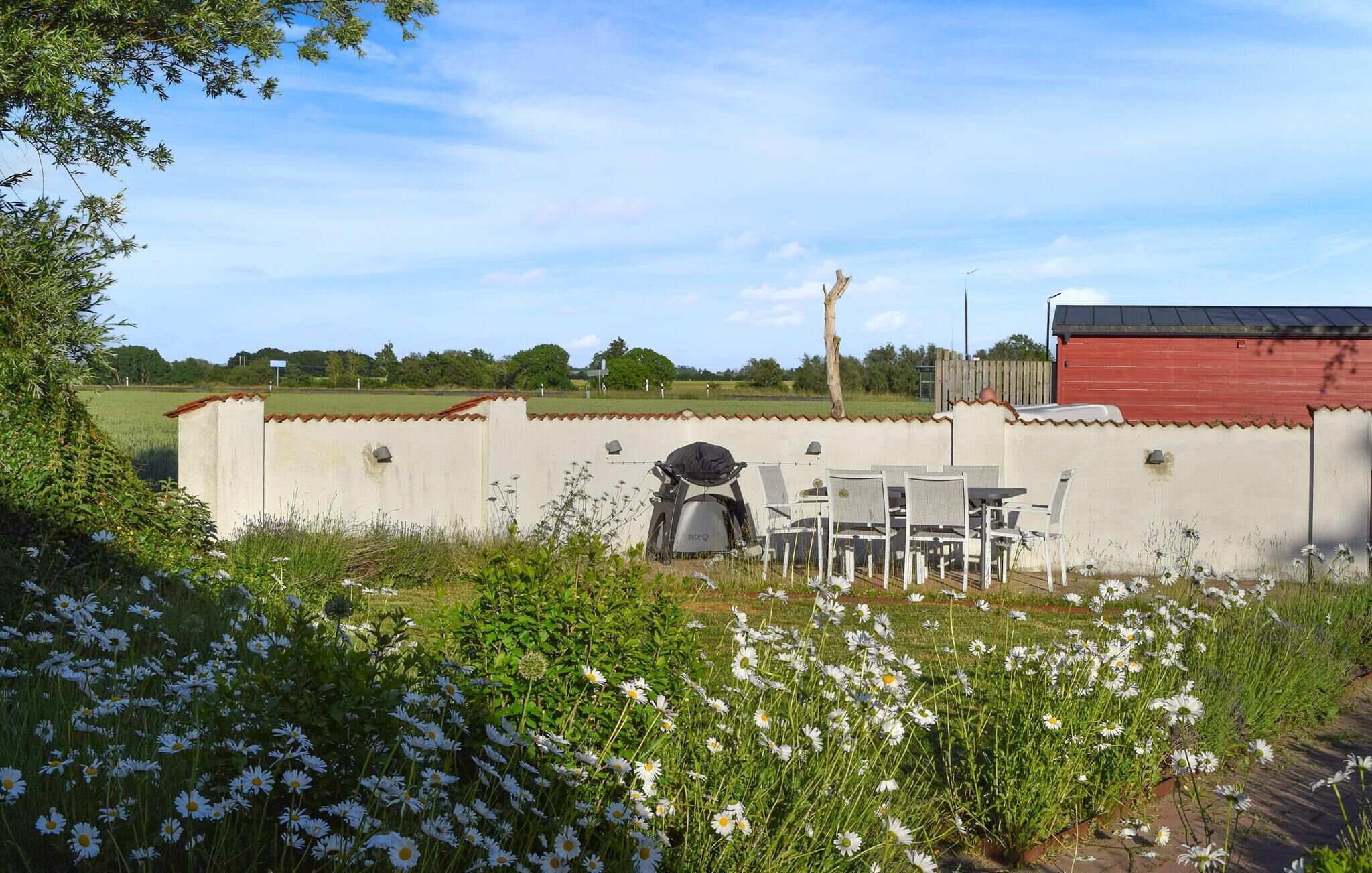 A garden with a white wall, a red building, and a table with chairs.