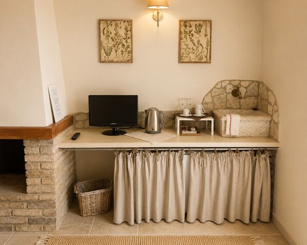 Un coin douillet avec une cheminée en pierre, un téléviseur à écran plat, un mur en pierre et une petite table sur laquelle se trouvent une bouilloire et des tasses.