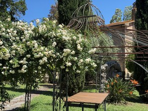 Un jardín con un pérgola cubierta de flores blancas, una estructura de piedra y una mesa de madera.