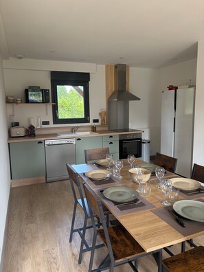 A modern kitchen with a dining area, equipped with a dishwasher, stove, and refrigerator. - Ô p'tit Normand: A peaceful, green spot near Honfleur (Genneville)