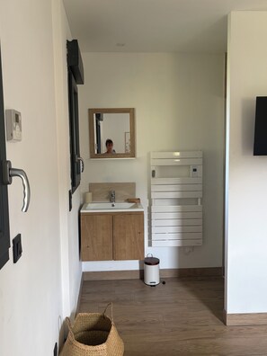 A bathroom with a wooden vanity, a mirror, a white toilet, and a wall-mounted heater. - Ô p'tit Normand: A peaceful, green spot near Honfleur (Genneville)