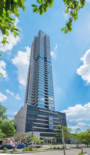 A tall, modern building with a prominent 'PETRA' sign, surrounded by greenery and parked cars. - Corporate Stays Petra Tower (Asunción)