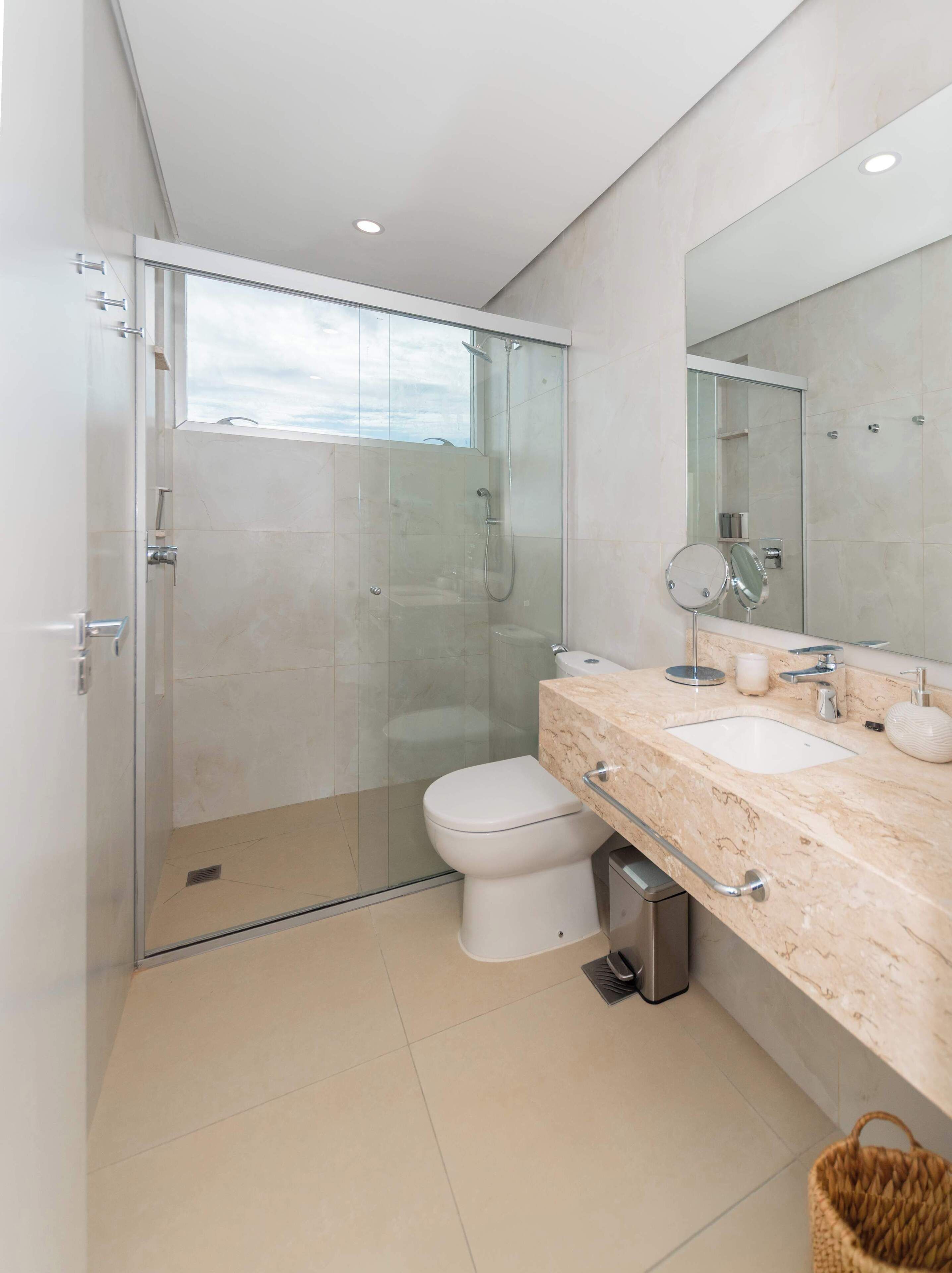 Une salle de bain moderne avec une douche à parois de verre, des toilettes blanches et un plan de toilette en marbre avec un lavabo et un miroir.