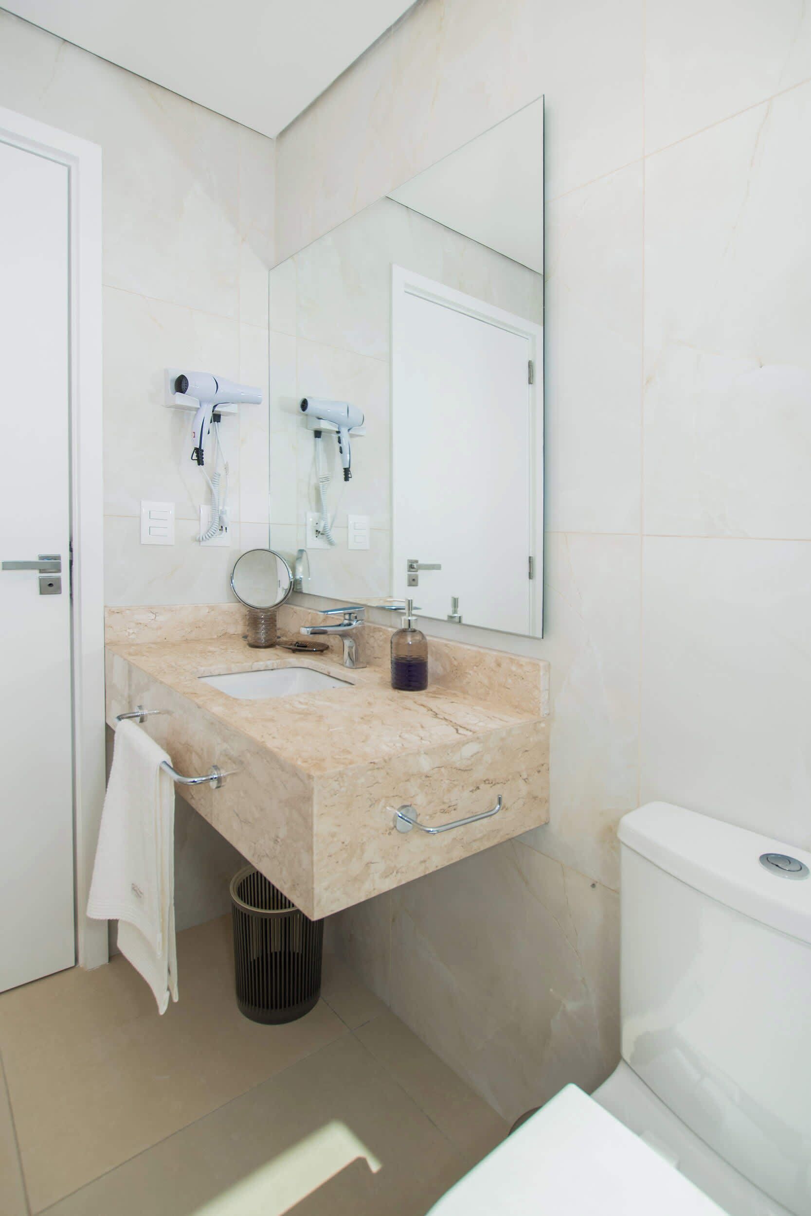 A bathroom with a marble sink, a mirror, two hair dryers, a trash can, and a toilet.