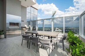 A modern outdoor dining area with a large table and chairs, a built-in grill, and a view of the cityscape. - Corporate Stays Petra Tower (Asunción)
