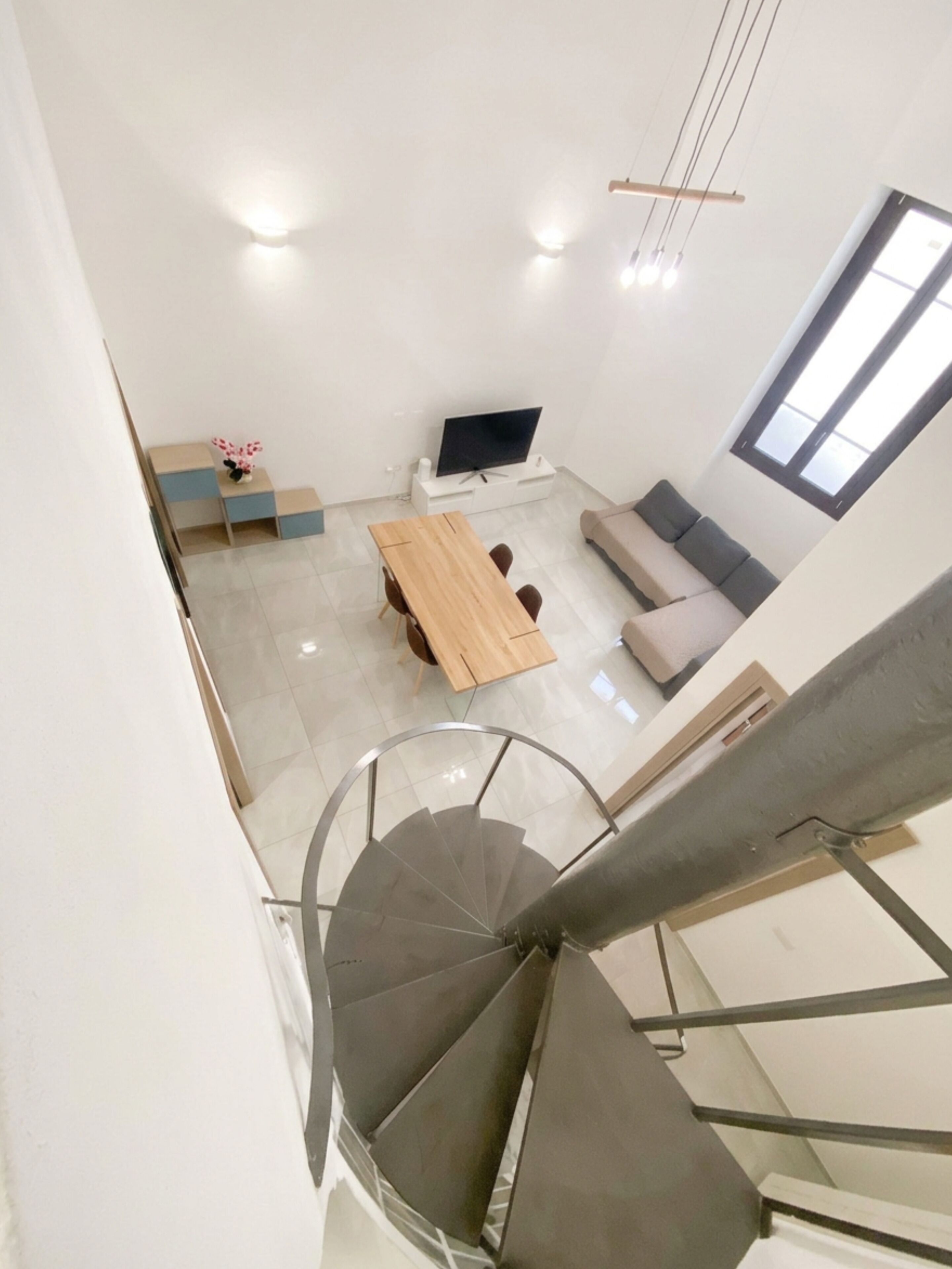 Uma sala de estar moderna com uma mesa de jantar de madeira, um sofá, uma televisão e uma escada.