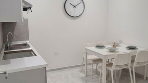 A modern kitchen with a built-in sink, white cabinets, a dining table with chairs, and a wall clock.