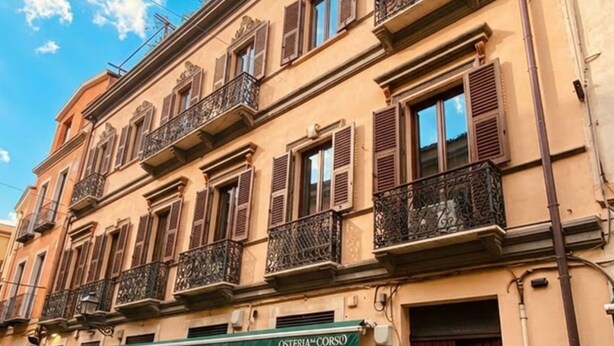 A multi-story building with a green awning labeled 'OSTERIA CORSO' and a dark brown door.