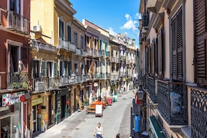 Une rue étroite bordée d’immeubles à étages, de balcons et d’espaces aménagés pour les terrasses.