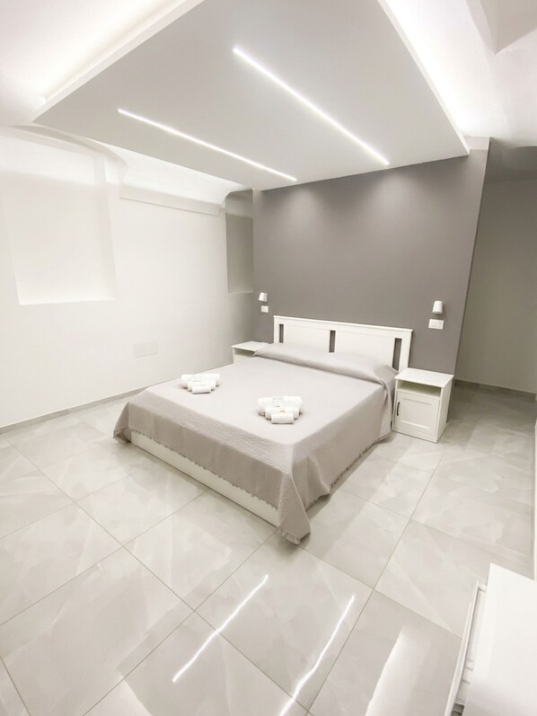 Un dormitorio moderno con techo inclinado, cama con cabecera blanca, mesitas de noche y un ventanal grande.