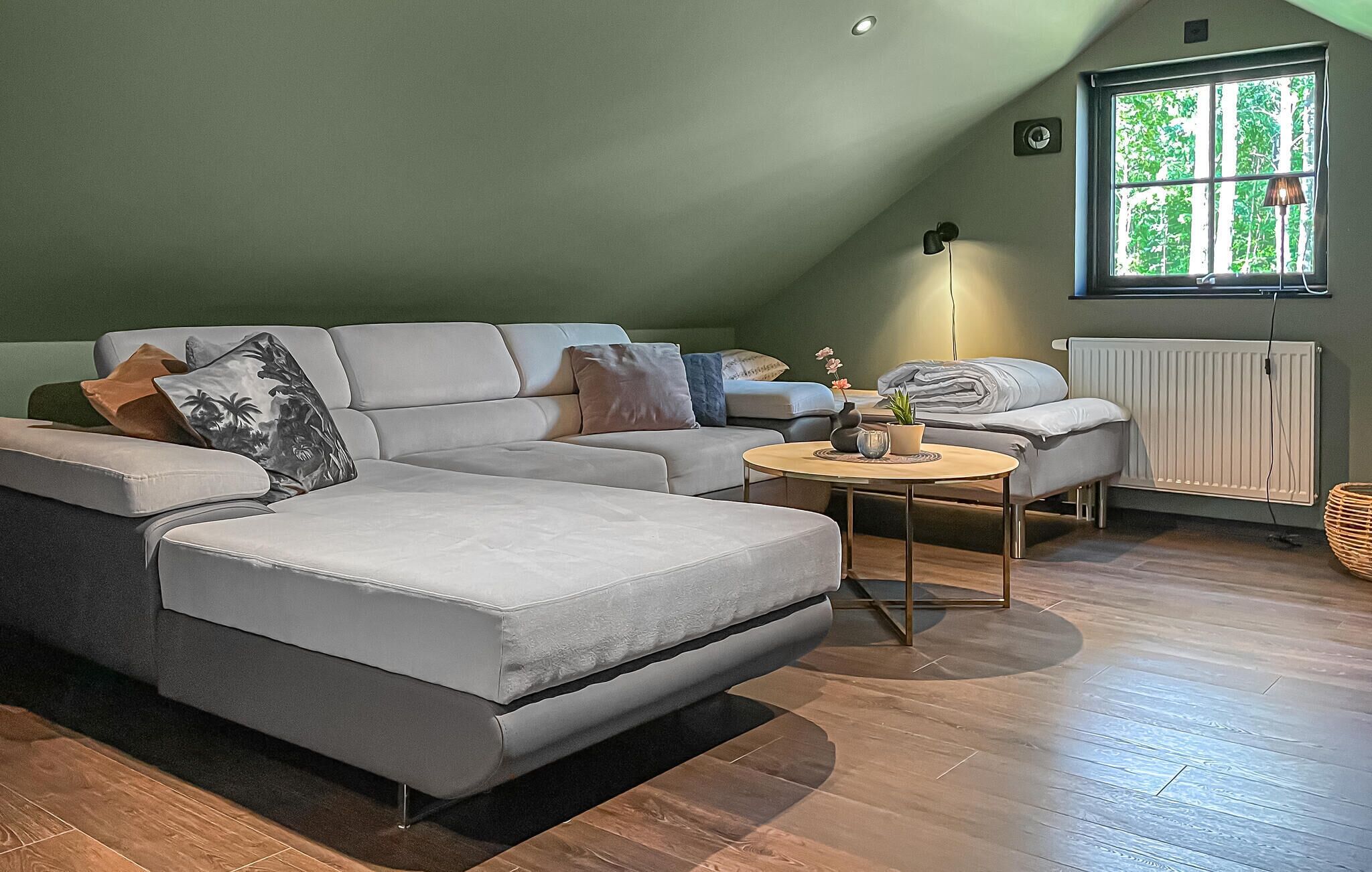 Une chambre moderne de style loft, avec un canapé d’angle, une petite table ronde et un radiateur.