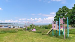 En legeplads med gynger og rutschebaner, en græsmark og et vandareal med både i baggrunden.