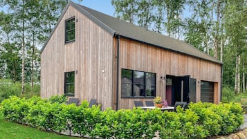 Une cabane en bois avec un toit en pente, de grandes fenêtres et une terrasse aménagée avec du mobilier d’extérieur.