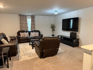 A living room with a sofa, armchair, coffee table, and a flat-screen TV mounted on the wall. - The Grand Haven 5BR 3BTR Family Retreat Sleeps 12. Spacious and Stylish (Cleveland)