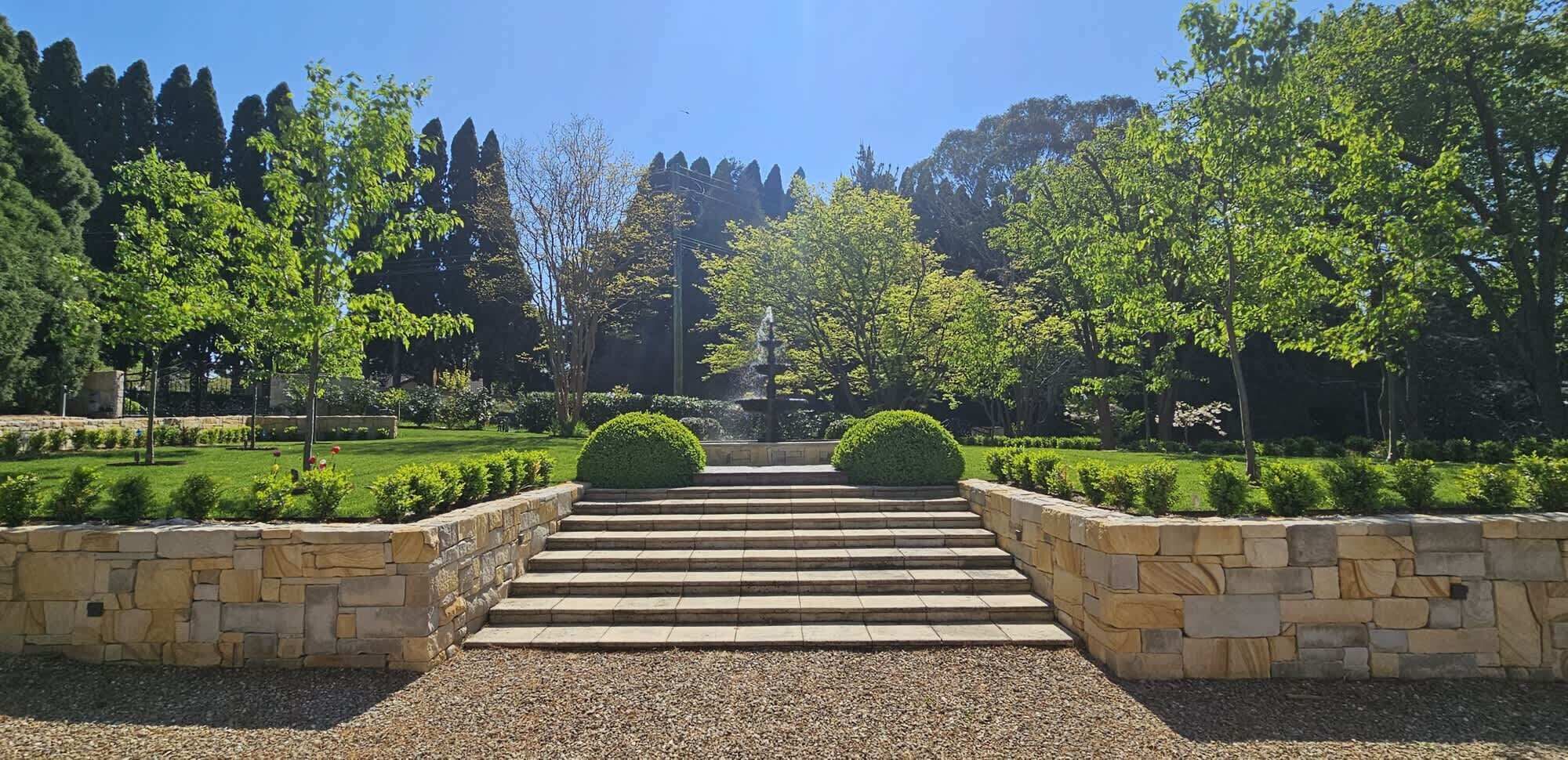 A stone pathway leading to a building entrance, surrounded by well-maintained greenery and trees.