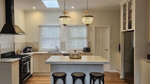 A modern kitchen with a central island, pendant lights, a stove, and a refrigerator. - Balnagowan, Garden Retreat 3-Bed Home in Moss Vale (Moss Vale)