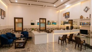Um saguão de hotel com balcão de recepção, área de estar e uma televisão.