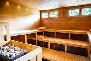 Una sauna con bancos de madera, una pila de piedra y ventanas con vistas al bosque.
