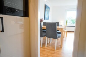 Ett modernt matområde med ett träbord och grå klädda stolar, en blå abstrakt målning på väggen och ett fönster med utsikt över grönområden.