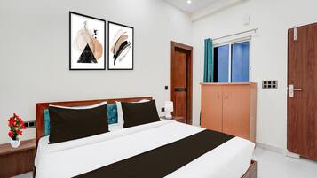 A hotel room with a bed, wooden wardrobe, a door, and a window with curtains.