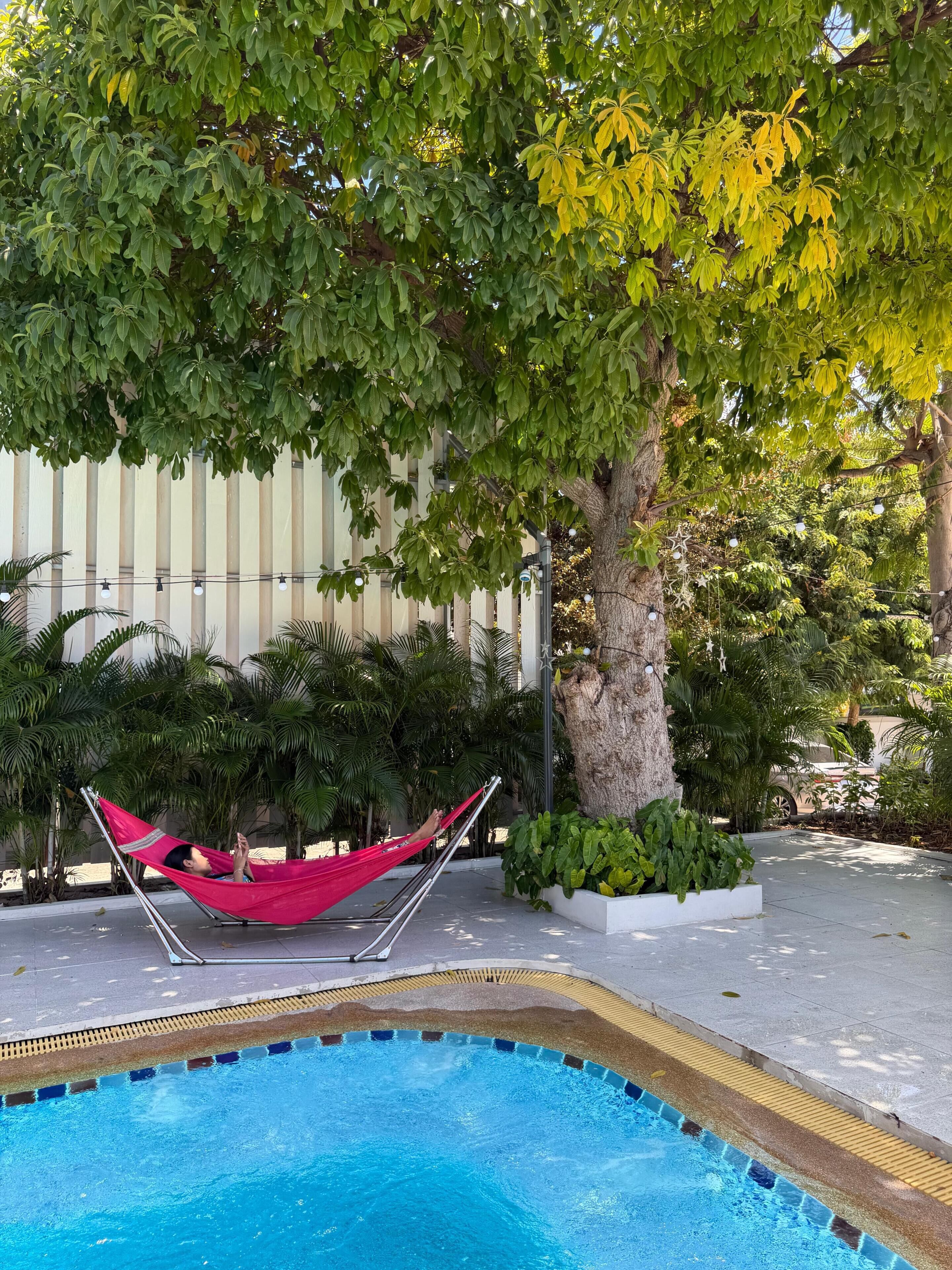 Zona de piscina con una hamaca, árboles y una valla.
