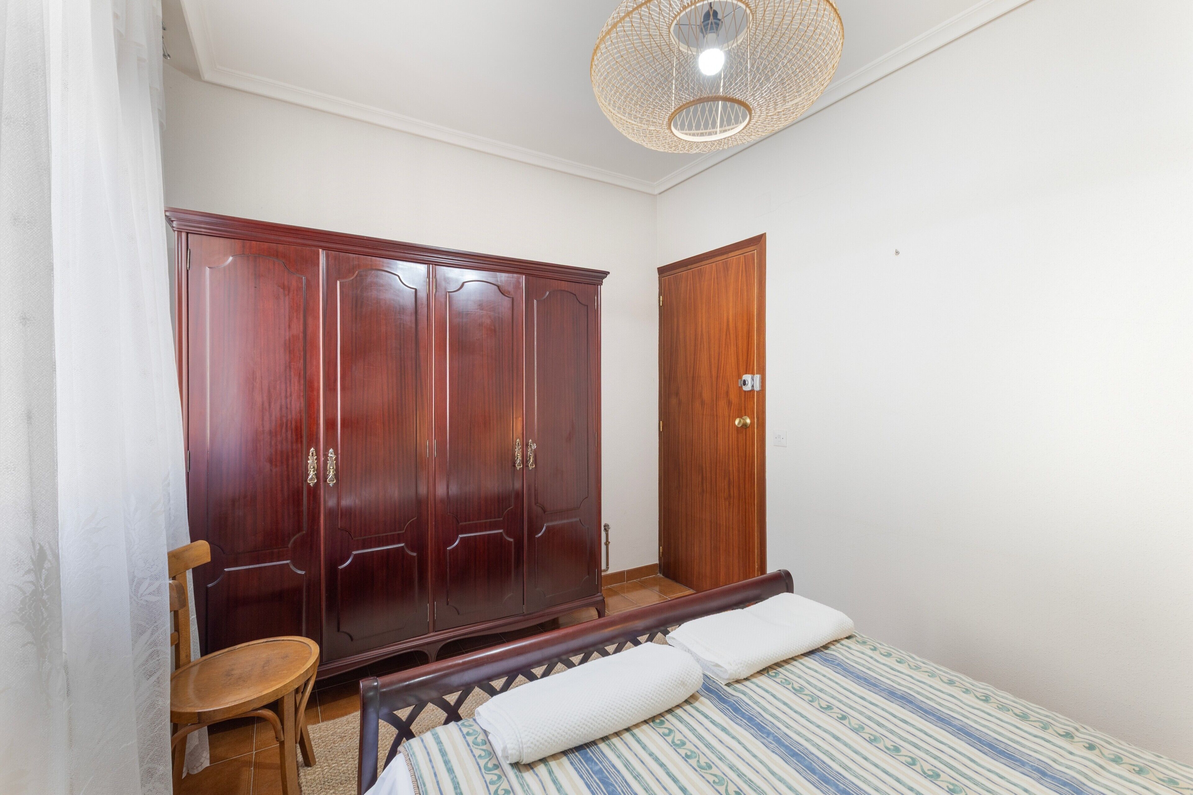 Un dormitorio con una cama, un armario de madera, una silla y una puerta.