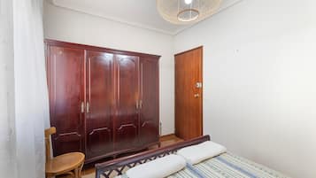 Een slaapkamer met een bed, een houten garderobe, een stoel en een deur.