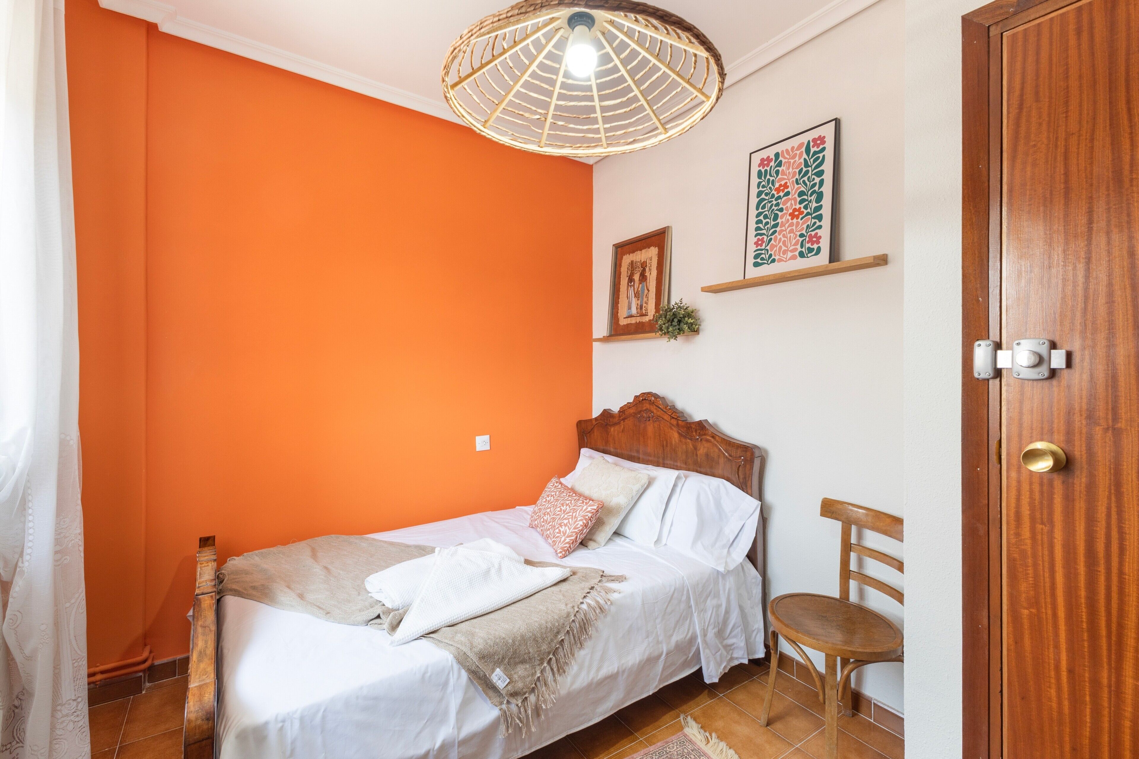 A room with a bed, a chair, a door, and a wall with a shelf.