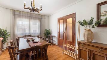 Een eetruimte met een houten tafel, stoelen, een kroonluchter en een deur met een ruit.