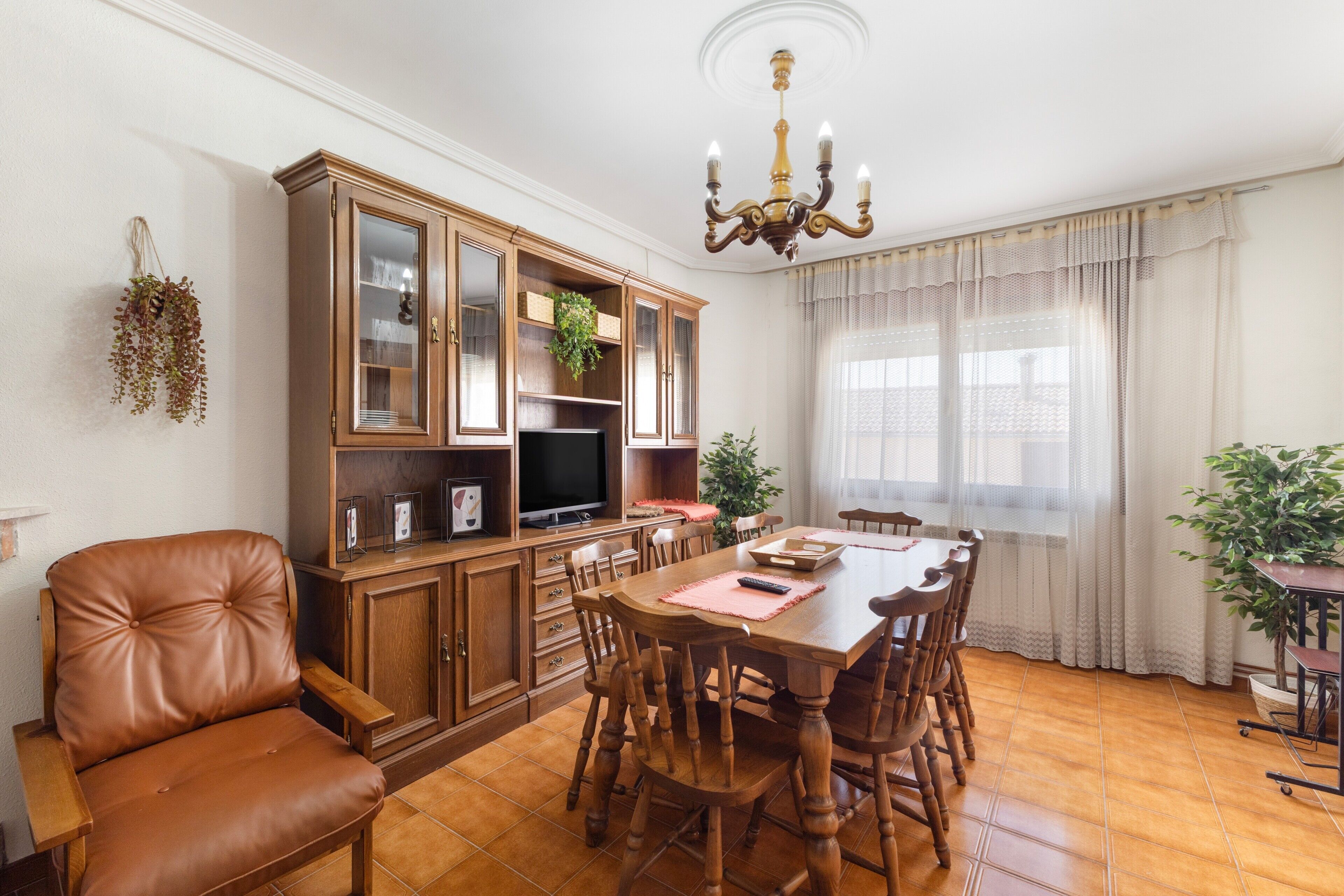 A dining area with a wooden table, chairs, a cabinet, and a television.