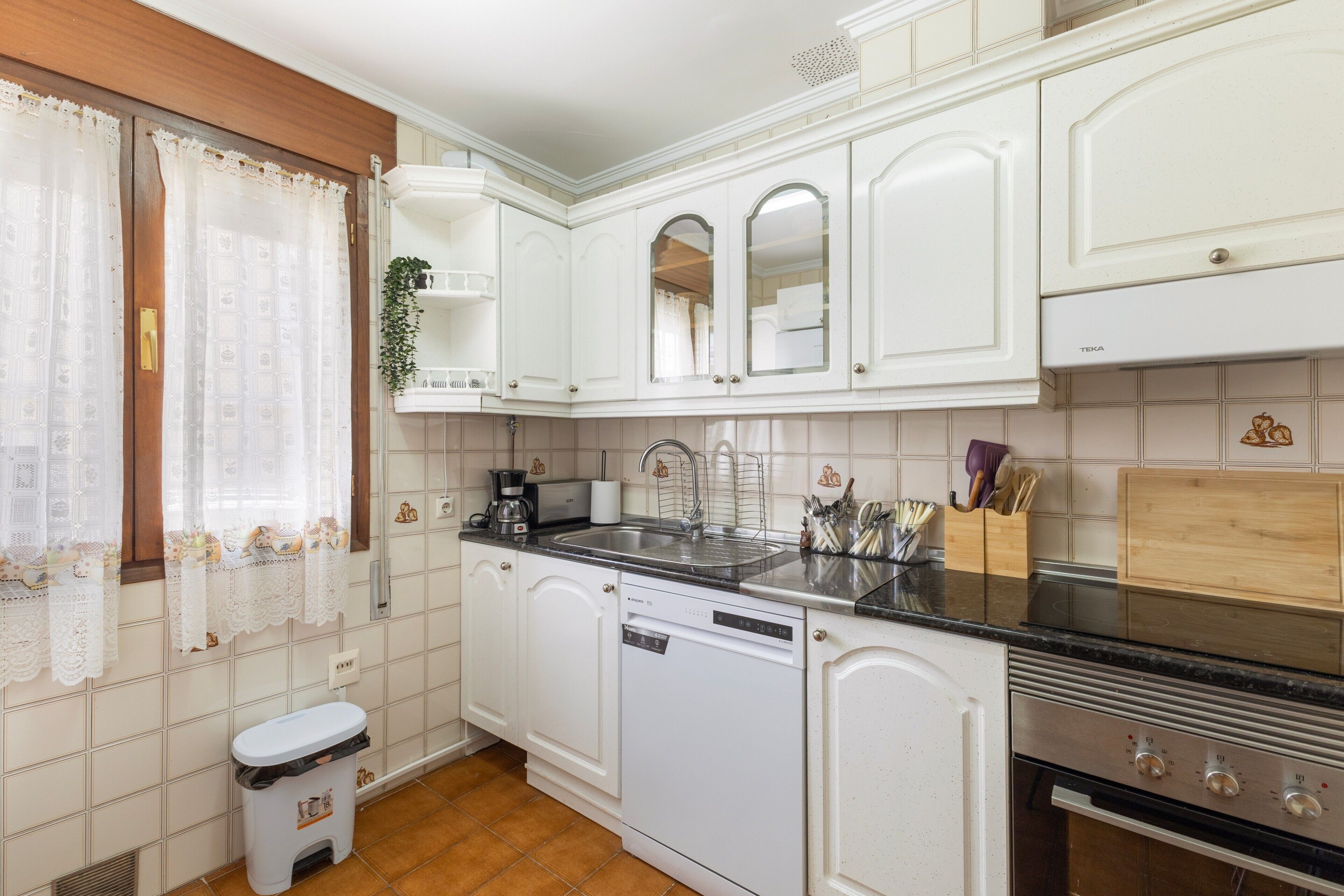 Una cocina compacta con armarios blancos, un lavaplatos de acero inoxidable, lavavajillas y horno integrado.